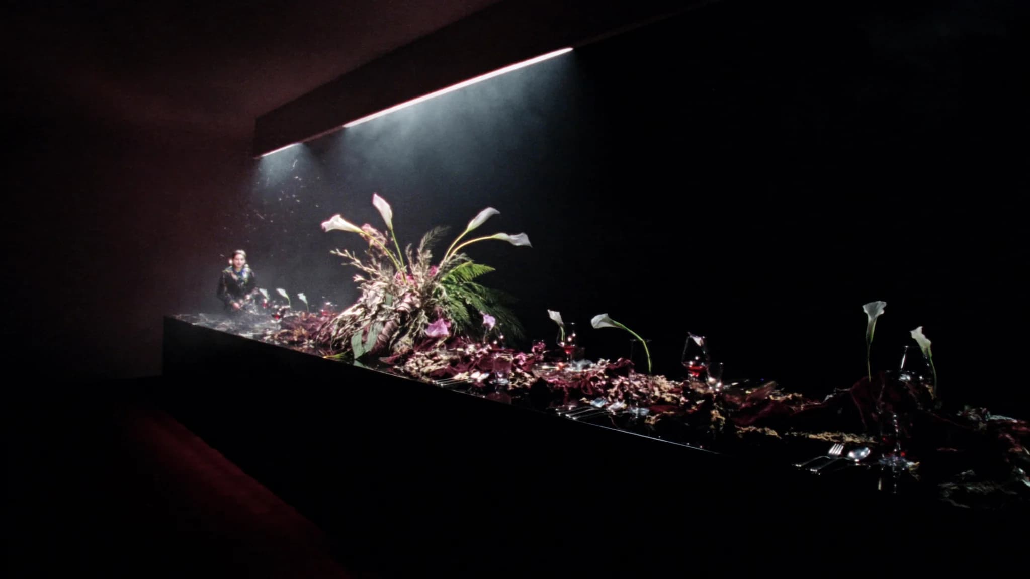 Long black banquet installation with sculptural flowers illuminated by a theatrical spotlight